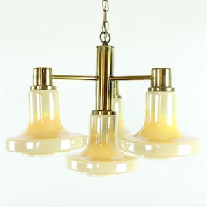 May include: A brass chandelier with four frosted glass shades. The shades are a pale yellow color and have a slightly iridescent finish. The chandelier has a simple, elegant design.