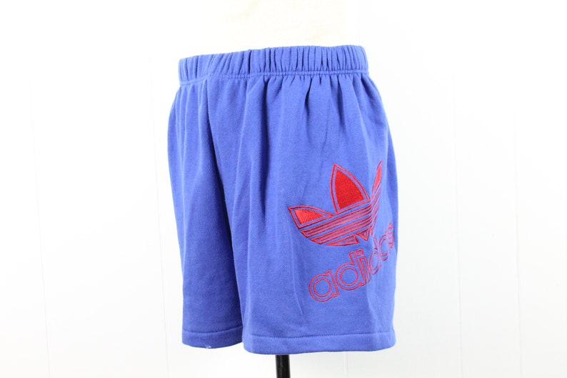 May include: Blue athletic shorts with a red Adidas logo embroidered on the right leg.