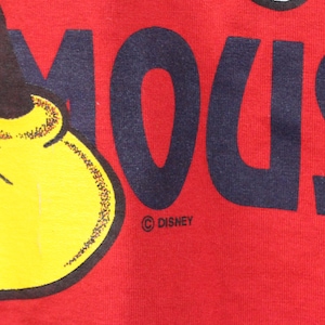 May include: Close-up of a red fabric featuring a partial image of Mickey Mouse's face and the word "MOUSE" in navy blue block letters. The Disney logo is visible.