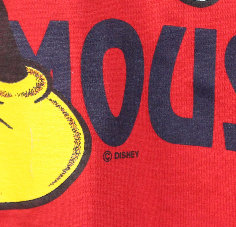 May include: Close-up of a red fabric featuring a partial image of Mickey Mouse's face and the word "MOUSE" in navy blue block letters. The Disney logo is visible.