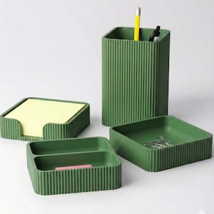 May include: A set of four green desk organizers. Includes a pencil holder with a yellow pencil, a square tray, a divided tray with a pink item, and a notepad holder with yellow sticky notes. The organizers have a ribbed design.