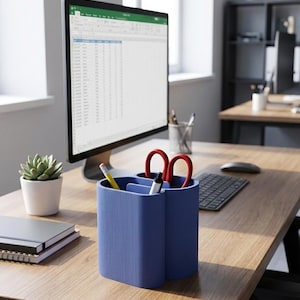 May include: A blue desk organizer with three compartments, holding a pencil, pen, and red scissors. The organizer sits on a wooden desk, next to a computer monitor displaying a spreadsheet. A small succulent in a white pot is also on the desk.