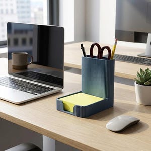 Puede incluir: Un organizador de escritorio azul y verde con un soporte para blocs de notas y un soporte para bolígrafos y lápices. El organizador está sobre un escritorio de madera junto a un portátil, una taza, un ratón y una pequeña planta en maceta.