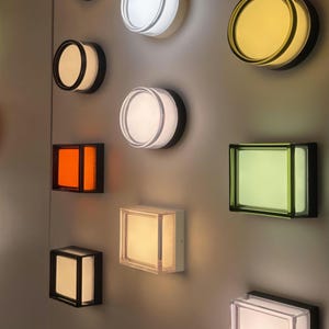 Pode incluir: Coleção de arandelas de parede modernas em várias formas e cores. As arandelas incluem designs circulares e retangulares com molduras pretas e interiores iluminados em branco, amarelo, laranja e verde.