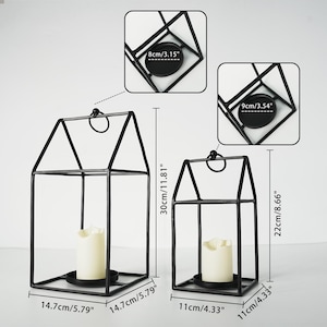May include: Two black metal candle lanterns. The larger lantern is 30cm/11.81" tall and 14.7cm/5.79" wide, and the smaller is 22cm/8.66" tall and 11cm/4.33" wide. Each lantern has a house-like shape with a handle and a candle holder.