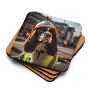 May include: A set of four square coasters with a cork backing. Each coaster features a photo of a brown and white dog wearing a construction helmet and a high-visibility vest. The dog is the focal point, set against a blurred urban background.