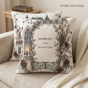 Könnte beinhalten: Zwei dekorative Kissen mit einem gotischen Schlossdesign. Die Kissen haben einen cremefarbenen Hintergrund mit einer gerahmten Illustration eines Schlosses, Rosen und dem Text "morally grey is my favorite color". Die Kissen liegen auf einem beigen Sofa.