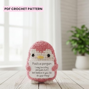 May include: A pink and white crocheted penguin holding a sign that reads "Positive penguin I may be a tiny penguin, but I bet believe in you. Go do your thing!" The text "PDF CROCHET PATTERN" is at the top.