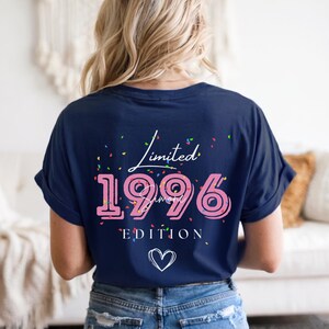 May include: Navy blue t-shirt with the text "Limited 1996 Edition" in pink and white. The design includes a heart and confetti-like accents. The shirt is a casual style.