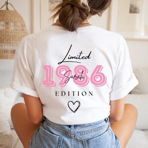 May include: White t-shirt featuring the text "Limited 1986 Sarah EDITION" in black and pink. A black heart is below the text. The shirt has a relaxed fit.
