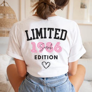 May include: White t-shirt with the text "LIMITED 1986 Sarah EDITION" in black and pink. A heart outline is below the text. The shirt is being worn by a person.