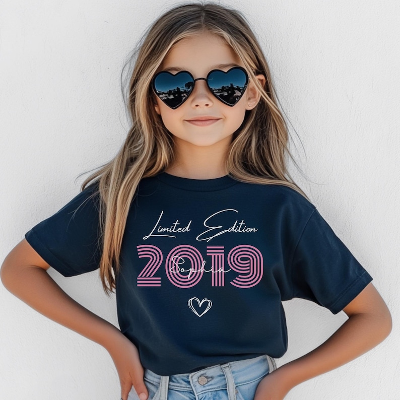 Pu&ograve; includere: Una t-shirt a maniche corte blu navy scuro con la scritta bianca Limited Edition, il numero 2019 a righe rosa, il nome Sophia in corsivo bianco e un grafico a forma di cuore bianco stampato al centro sulla parte anteriore.