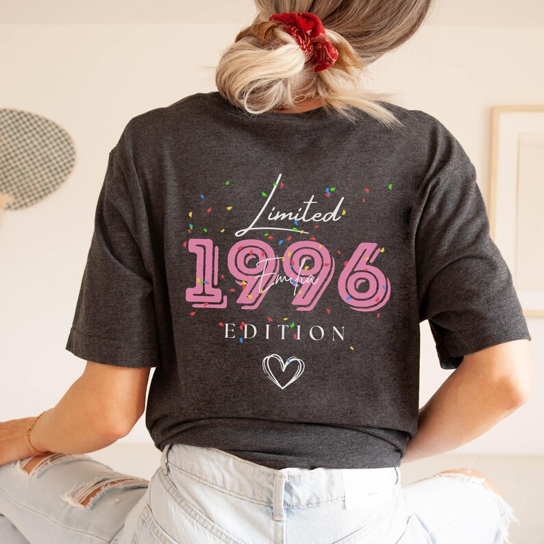 May include: Dark gray t-shirt with the text "Limited 1996 Edition" in pink and white. The design includes confetti and a heart symbol. The shirt is a casual style.