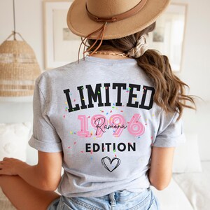 May include: A light gray t-shirt with the text "LIMITED EDITION 1996 Ramona" in black and pink, with confetti and a heart graphic. The shirt is worn by a person wearing a hat and jeans.