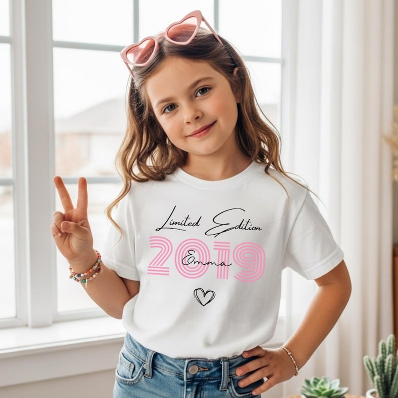 Pu&ograve; includere: Una t-shirt bianca a maniche corte con la scritta Limited Edition in corsivo nero, il numero 2019 in carattere rosa a righe, il nome Emma in corsivo nero e il contorno di un piccolo cuore nero. La maglietta &egrave; abbinata a jeans in denim blu.