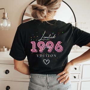 May include: Black t-shirt with the text "Limited 1996 Edition" in pink and white. The design includes confetti and a heart symbol. The shirt is a casual wear item.