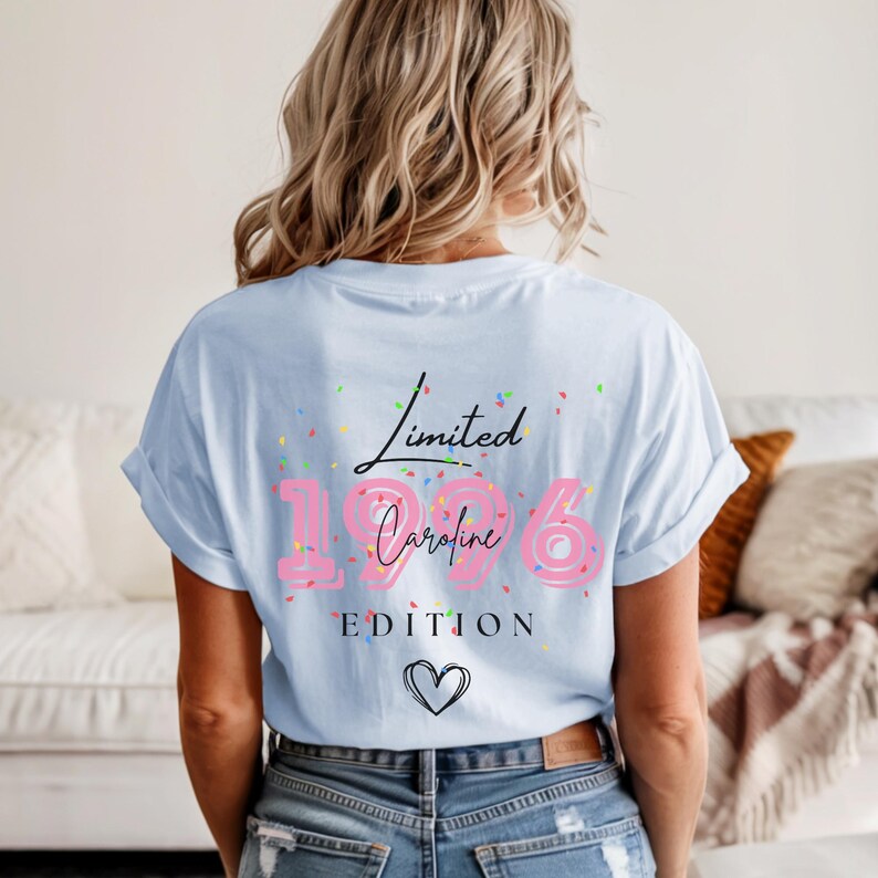 May include: Light blue t-shirt with the text "Limited Caroline 1996 Edition" in pink and black. The shirt has a heart graphic and colorful confetti. The model is wearing blue jeans.
