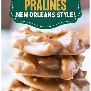 May include: A stack of Southern Pecan Pralines, New Orleans style. The candies are a light brown color with a glossy finish, and appear to be made with pecans. The image includes a green and white sign that says "Southern Pecan Pralines, New Orleans Style!"