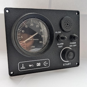 May include: Black marine instrument panel with a central gauge displaying RPM, labeled 'VOLVO PENTA'. Features include a speaker, toggle switches for 'GLOW' and 'ALARM TEST', and a 'POWER ON/OFF' switch. A large 'START' button is also present.