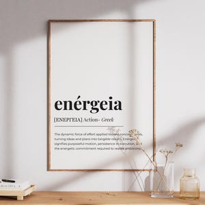 Könnte beinhalten: Ein gerahmter Druck mit dem Wort "enérgeia" in Schwarz, darunter eine griechische Übersetzung und Definition. Der Druck ist in einem Holzrahmen, an einer weißen Wand. Eine kleine Vase und eine Flasche stehen auf einer Holzoberfläche.