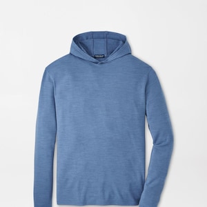 May include: A long-sleeve hooded pullover shirt in a heathered medium blue color. The garment features a hood with a visible interior seam and a small dark rectangular brand label sewn into the inner neckline area with white text.