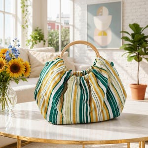 May include: A striped fabric handbag with a wooden handle. The bag features vertical stripes in green, yellow, and white. The handle is a light-colored wood. The bag is sitting on a marble table.