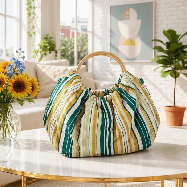 May include: A striped fabric handbag with a wooden handle. The bag features vertical stripes in green, yellow, and white. The handle is a light-colored wood. The bag is sitting on a marble table.