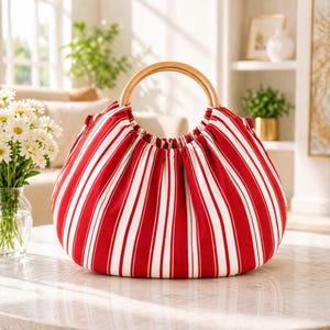 May include: A round red and white striped handbag with a wooden handle. The bag is made of fabric and has a gathered top. The handle is a light brown color and is circular in shape. The bag is sitting on a table.