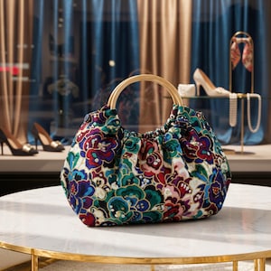 May include: A floral print handbag with wooden handles. The bag features a vibrant pattern of red, blue, and green flowers on a dark background. The handles are made of light-colored wood, and the bag sits on a marble table.