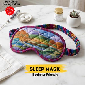 May include: A quilted sleep mask with a landscape design in shades of green, blue, and brown. The mask has a purple border and a colorful elastic strap. Text on the image reads "SLEEP MASK Beginner Friendly".