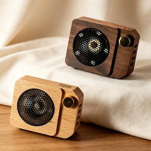 May include: Two rectangular portable speakers with wooden housings, one in a light wood tone and one in a dark wood tone. Each features a circular black metal mesh speaker grille, a gold-colored circular knob, and the name Benjamin printed on top.