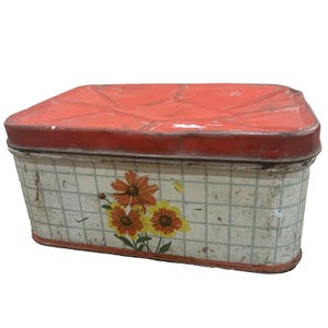 Può includere: Scatola di latta rettangolare vintage con coperchio rosso e corpo a scacchi bianchi e grigi. Il corpo presenta un motivo floreale con fiori arancioni e gialli. La scatola mostra segni di usura.