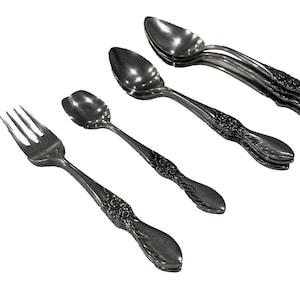 May include: A collection of antique silverware, including forks and spoons, with ornate floral detailing on the handles. The silverware is made of a shiny, silver-colored metal and is arranged on a white background.