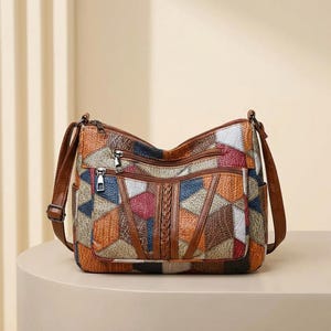 May include: A multi-colored shoulder bag featuring a patchwork design with textured panels in shades of brown, red, blue, and white. The bag includes two front zippered pockets, a braided leather accent, and an adjustable brown shoulder strap.