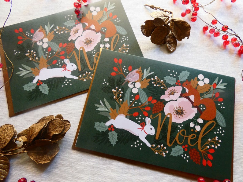 May include: Two green Christmas cards with gold lettering that says "Noel". Each card features a white rabbit, a squirrel, and a robin surrounded by red berries, flowers, and greenery.