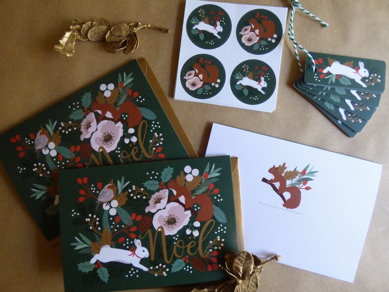 May include: A set of Christmas cards and gift tags featuring a green background with white rabbits, red squirrels, and red berries. The cards and tags have a gold foil accent and the text "Noel" in gold lettering.