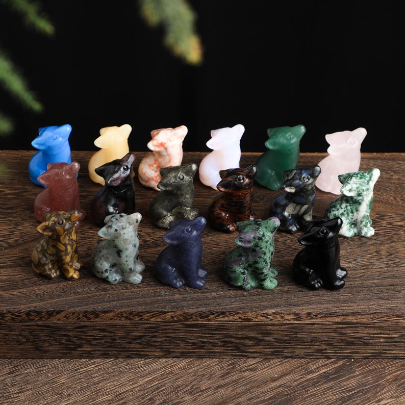 May include: A collection of small, carved stone dog figurines in various colors, including blue, green, pink, and black. The figurines are arranged on a dark wooden surface.