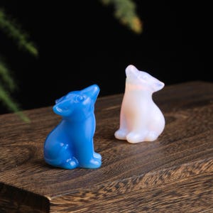 May include: Two small, carved wolf figurines. One is a vibrant blue, the other is a translucent white. Both are posed with their heads tilted upwards. They are displayed on a dark wooden surface.