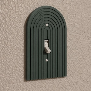 May include: A dark green arched light switch plate featuring a series of concentric vertical grooves. The plate is secured with two silver screws and surrounds a standard white toggle switch with the word OFF printed on the lever.