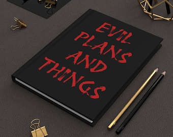 Könnte beinhalten: Ein schwarzes Notizbuch mit den Worten "EVIL PLANS AND THINGS" in roter Schrift. Goldene und schwarze Bleistifte sowie goldene Büroklammern sind um das Notizbuch auf einer dunkelgrauen Oberfläche angeordnet.