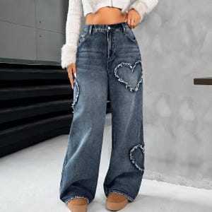 Peut inclure: Jean large taille haute dans un délavage bleu foncé avec des découpes en forme de cœur effilochées sur le devant. Ce pantalon en denim présente une fermeture classique à bouton et fermeture éclair, cinq poches et des bords effilochés.