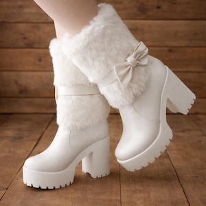 May include: White platform boots with faux fur trim and a bow detail. The boots have a chunky heel and a lug sole. The boots are made of a smooth, white material. The boots are approximately 5 inches tall.