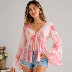 May include: A long-sleeved blouse featuring a pink and white marble-like pattern with gold veining. The garment has a deep V-neckline with a front tie closure and flared bell sleeves, paired with light blue denim shorts with a frayed hemline.