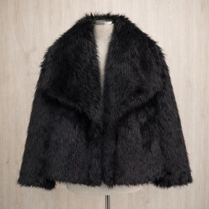 May include: A black faux fur jacket with a wide collar. The jacket is displayed on a mannequin against a light wood-grain background. The jacket has a soft, textured appearance.