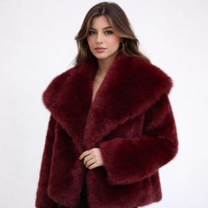 May include: A burgundy faux fur coat with a wide collar. The coat has long sleeves and a soft, plush texture. The coat is a deep red color and appears to be warm and cozy.