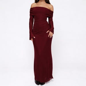 Puede incluir: Un vestido largo burdeos con hombros descubiertos. El vestido de manga larga presenta un corpiño fruncido y una falda fluida. El vestido está hecho de una tela suave y drapeada, adecuado para eventos formales. El vestido mide aproximadamente 150 cm de largo.