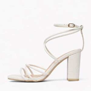 May include: White strappy heeled sandal with a square toe and ankle strap. The sandal features multiple thin straps that wrap around the foot and ankle. The block heel is approximately 3.5 inches high.