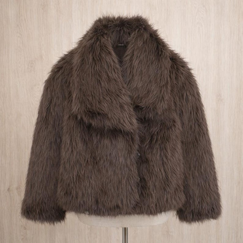 May include: A brown faux fur jacket with a wide collar. The jacket has a button closure and a soft, textured appearance. The garment is displayed on a mannequin against a light wood background.