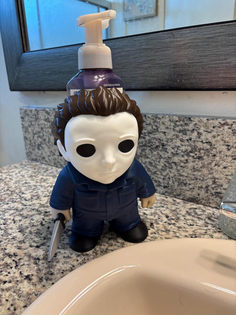 Peut inclure: Un distributeur de savon repr&eacute;sentant une figurine avec un masque blanc, des cheveux bruns et une combinaison bleue. La figurine tient un petit couteau argent&eacute; dans une main. Une pompe transparente est fix&eacute;e sur le flacon de savon violet.