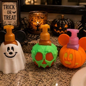 Peut inclure: Trois distributeurs de savon décoratifs sur le thème d'Halloween. L'un est un fantôme blanc avec des oreilles noires, l'autre une pomme orange avec de la mélasse verte, et le troisième une citrouille orange avec des oreilles et une pompe rose.